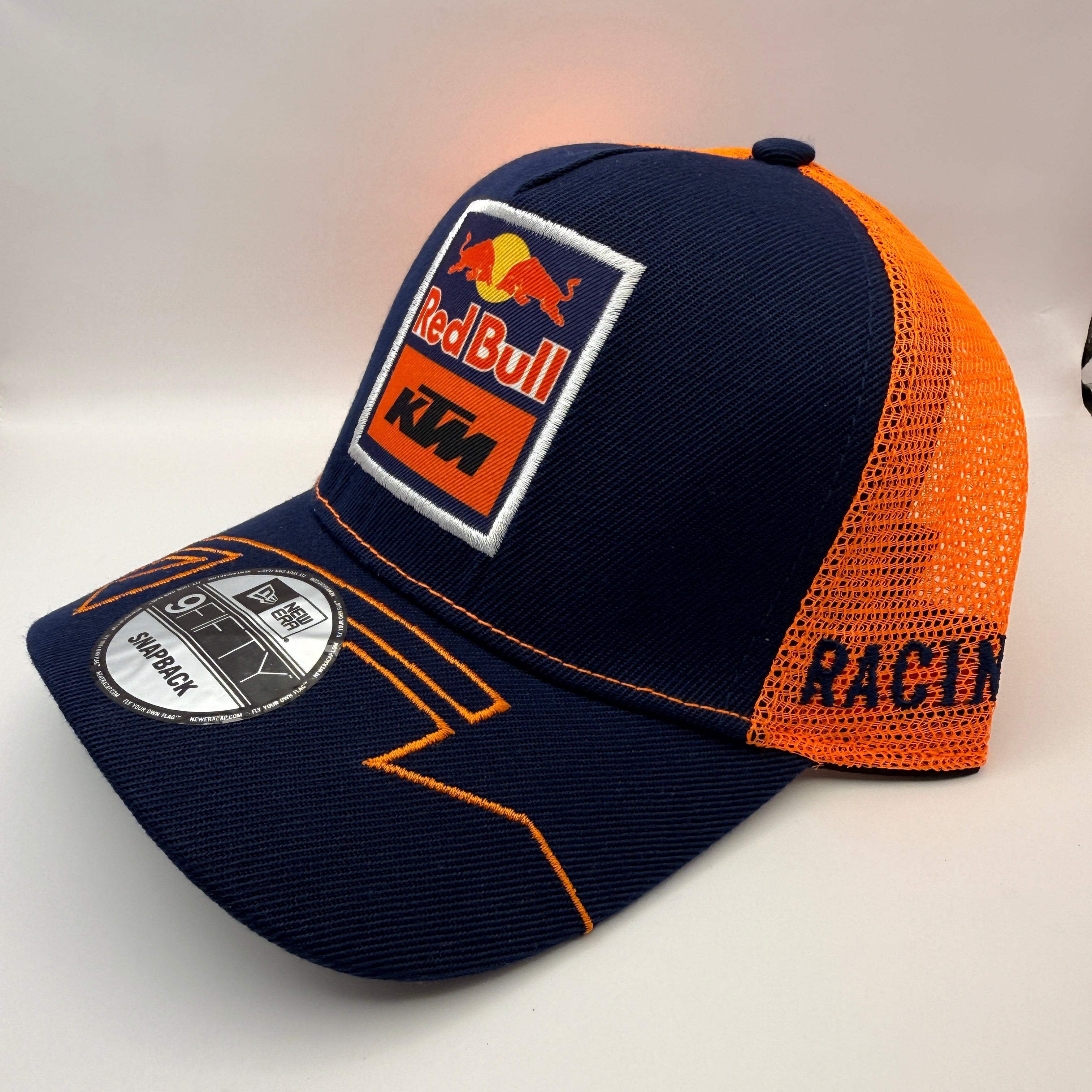 A navy blue and orange New Era 9FIFTY trucker cap featuring a Red Bull KTM patch on the front and 'RACING' text on the side, displayed on a light gray background.